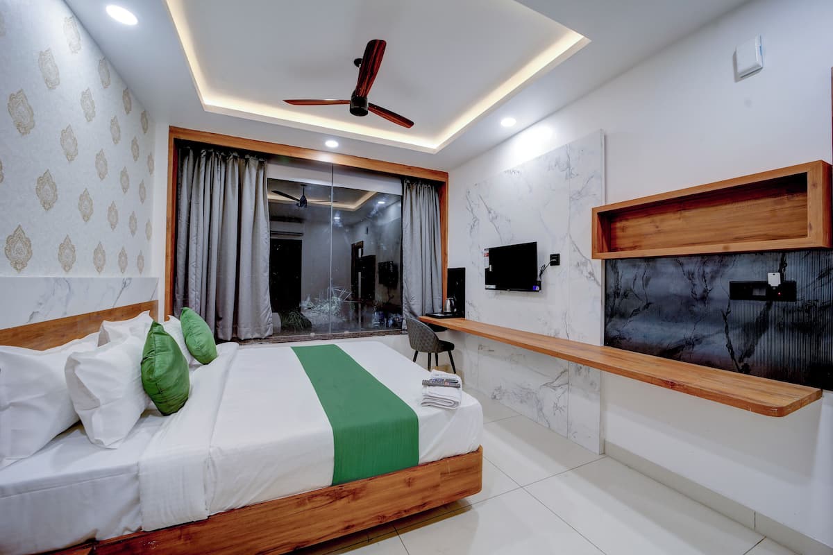 A modern bedroom with a bed, green pillows, a ceiling fan, a TV, and a wooden shelf.