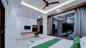 A modern hotel room with a large bed, a ceiling fan, a TV, and a view of the outside. - The Byke Boutique Urban Nest (Bhopal)