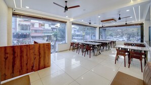 A modern dining area with multiple tables and chairs, large windows with city views, ceiling fans, and recessed lighting. - The Byke Boutique Urban Nest (Bhopal)