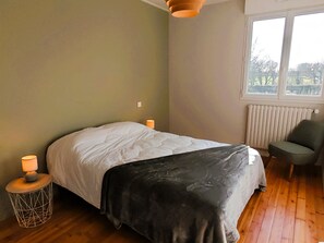 Ein Schlafzimmer mit Bett, Stuhl, Fenster und Heizkörper.