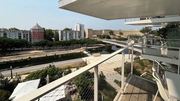 En modern byggnad med en takterrass som erbjuder utsikt över en flod och stadens silhuett.