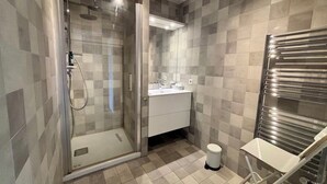 Ett modernt badrum med en duschavdelning med glasväggar, en vit tvättställ och en handduksställning.