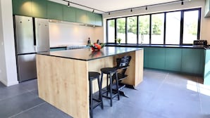 A modern kitchen with a central island, black bar stools, and large windows. - Ferme Valentour 24 beds, ideal for families and corporate seminars. (Gesves)