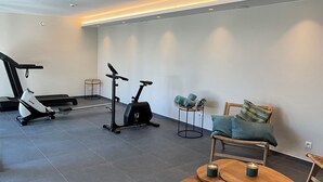 A modern gym with exercise equipment, a wooden bench, and a small table with candles. - Ferme Valentour 24 beds, ideal for families and corporate seminars. (Gesves)