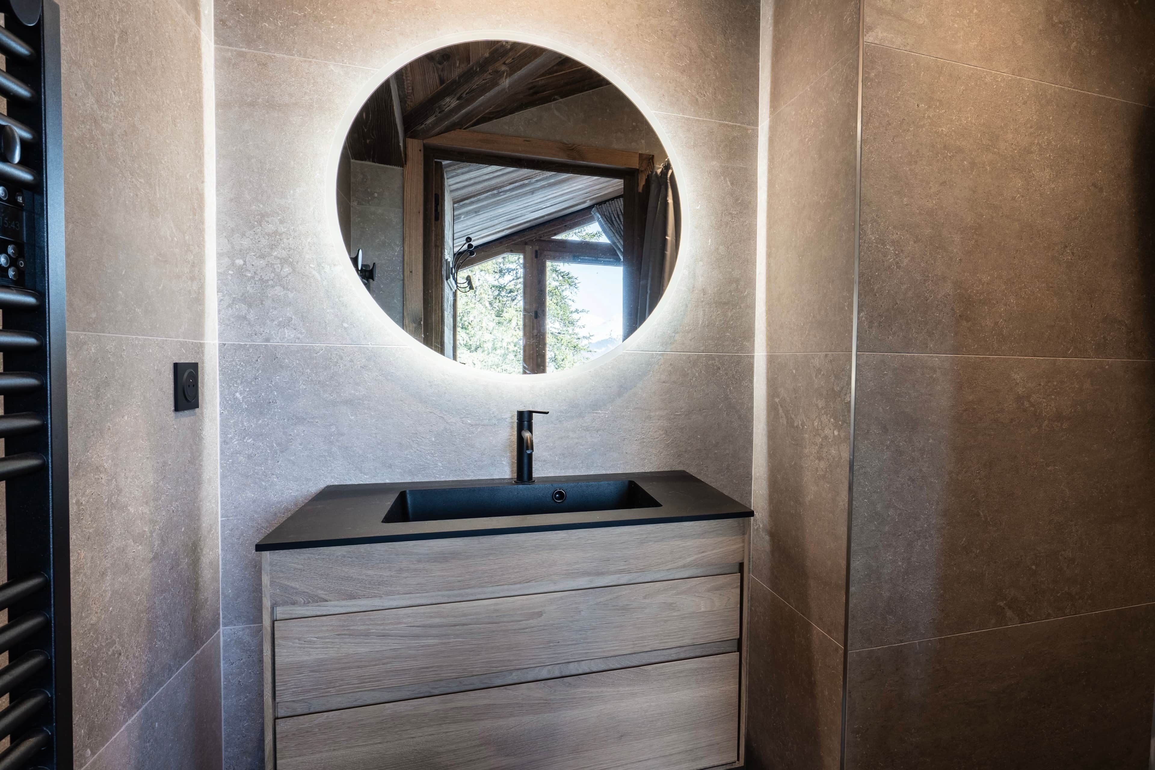 A bathroom with a round mirror, a sink, and a wooden cabinet.