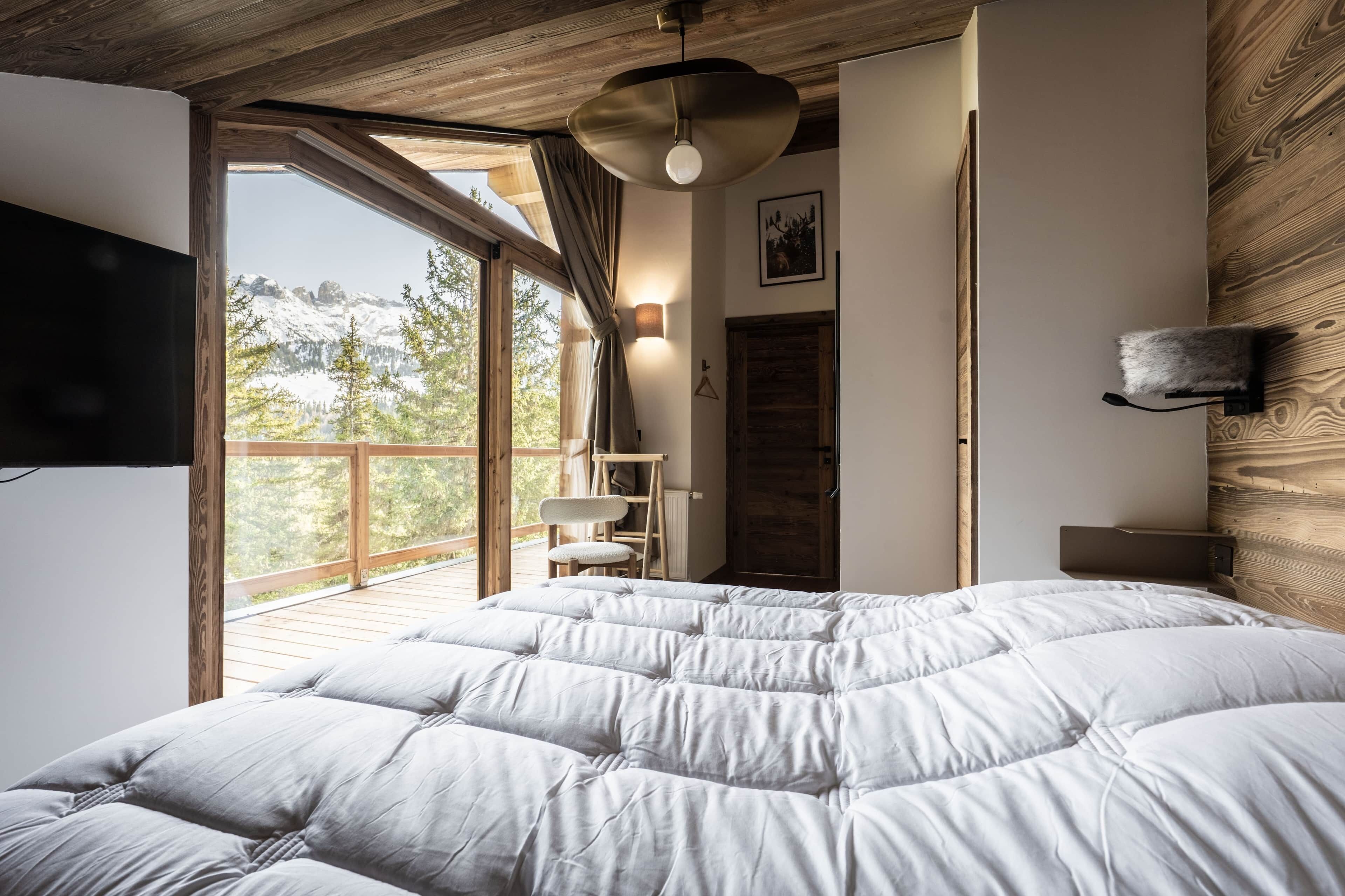 Un dormitorio con una cama grande, techo de madera, vistas a las montañas y un balcón.