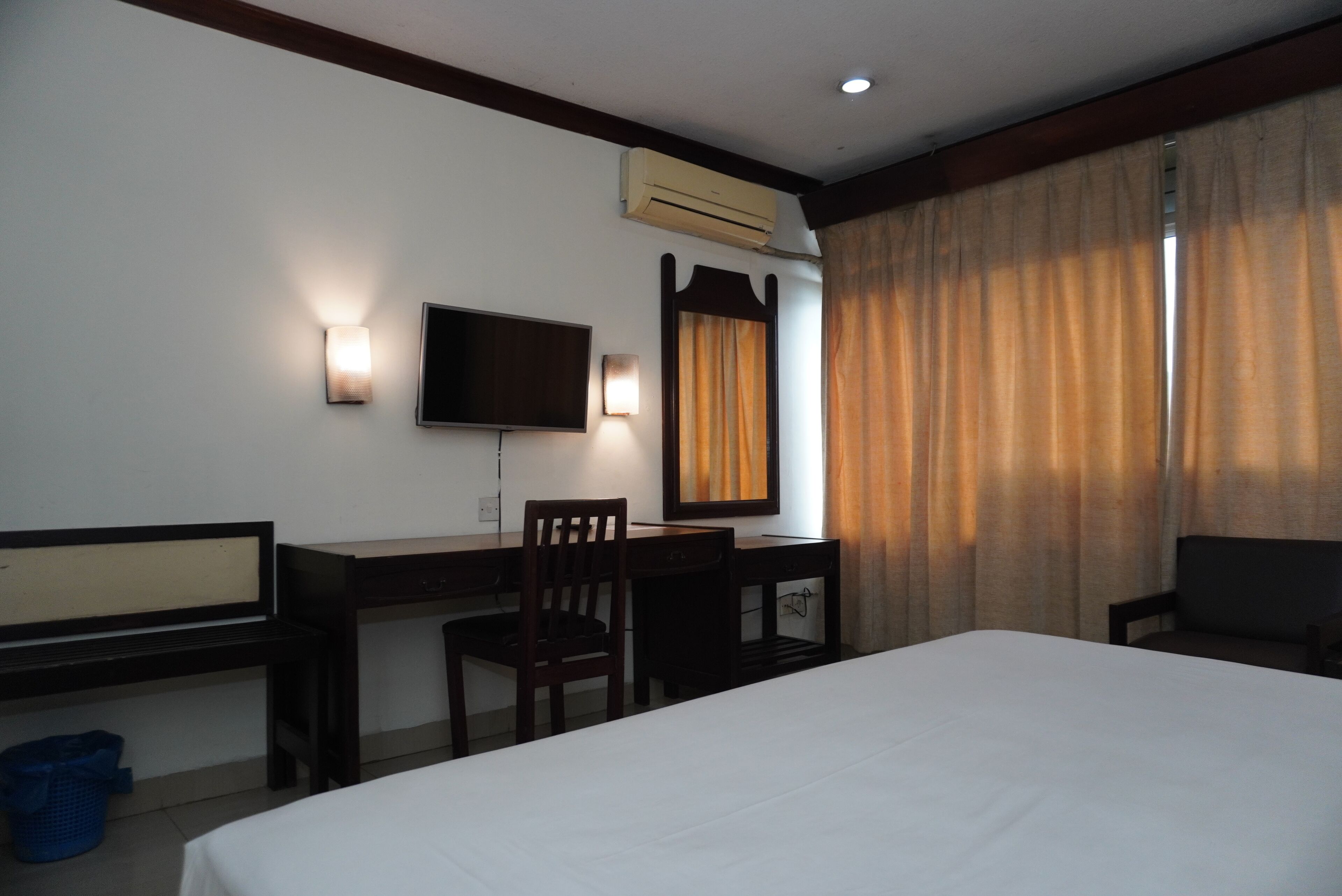 Habitación de hotel con cama, escritorio, silla, televisor y cortinas.