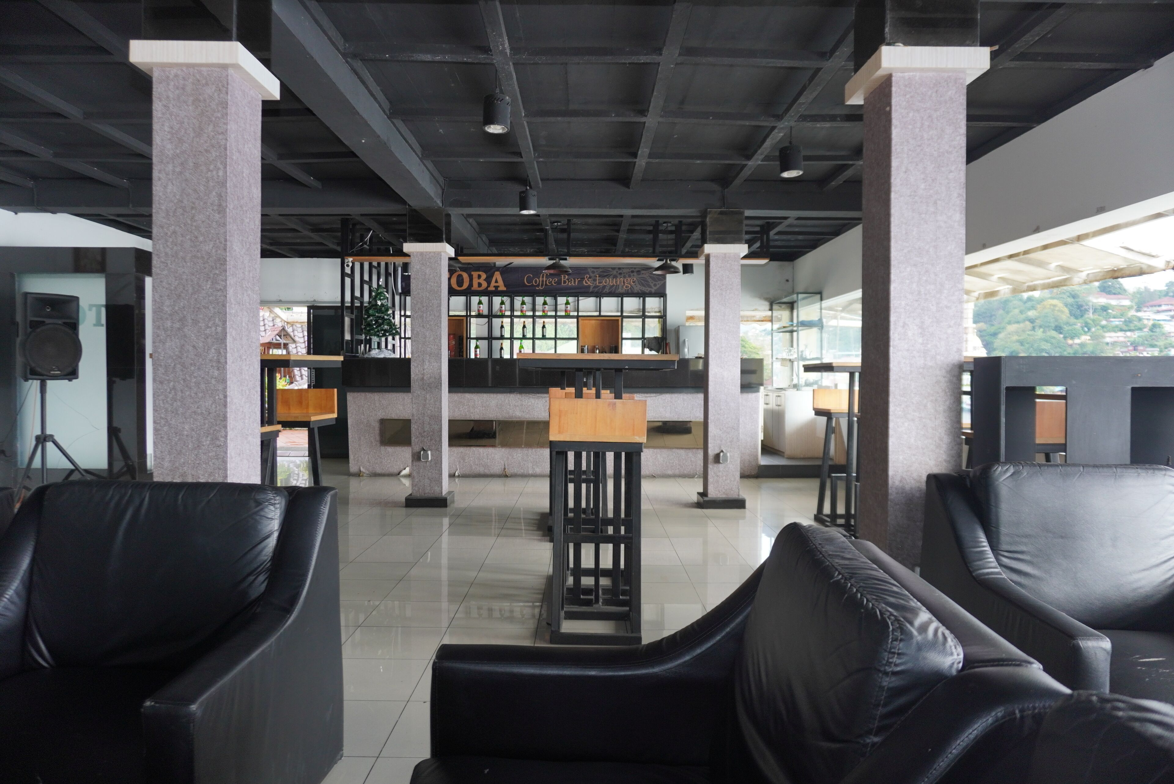 A modern interior with black leather chairs, a coffee bar, and a sign reading "OBA Coffee Bar & Lounge".