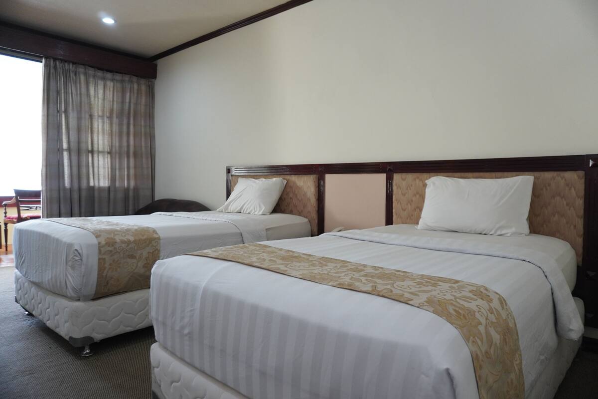 A hotel room with two beds, a large window with curtains, and a view of the outdoors.