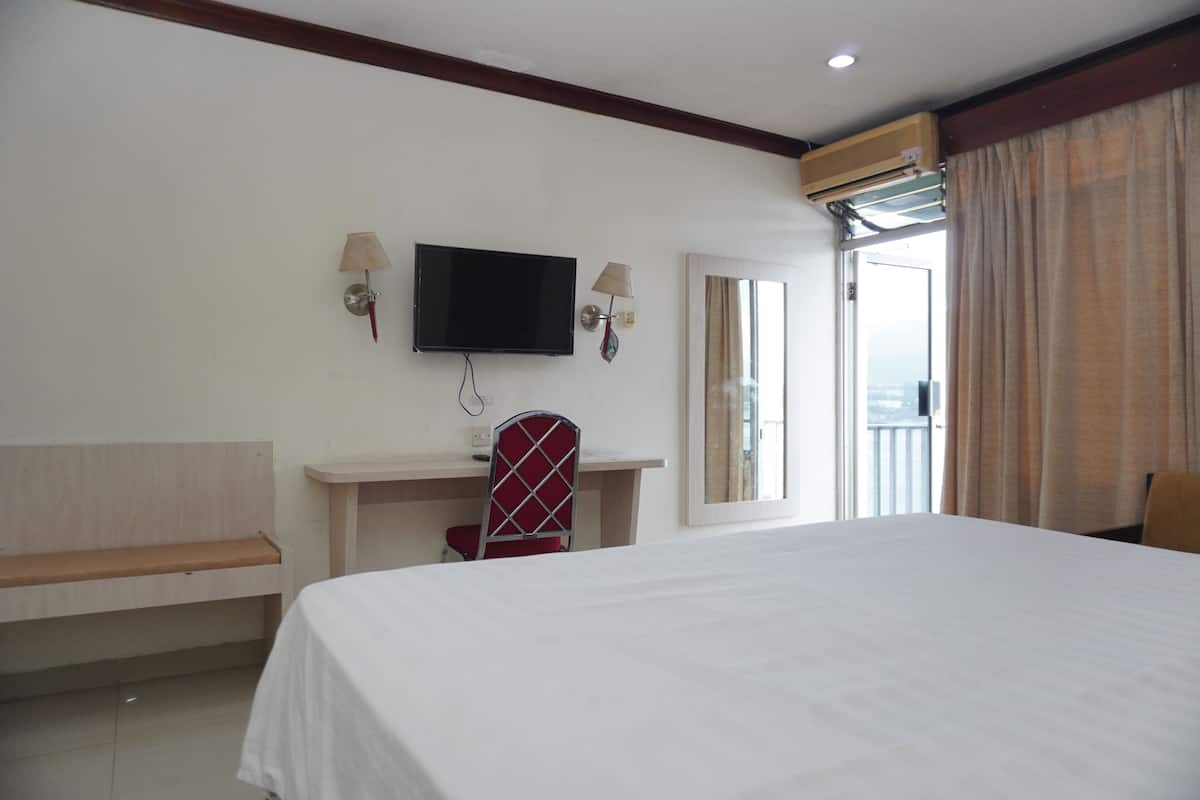 A hotel room with a bed, a desk, a chair, a television, and a window with curtains.