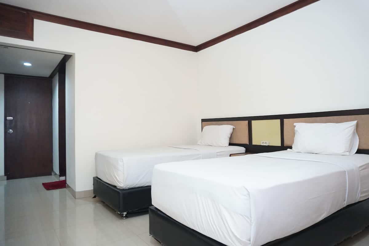 A hotel room with two single beds, a wooden headboard, a door, and a red mat on the floor.