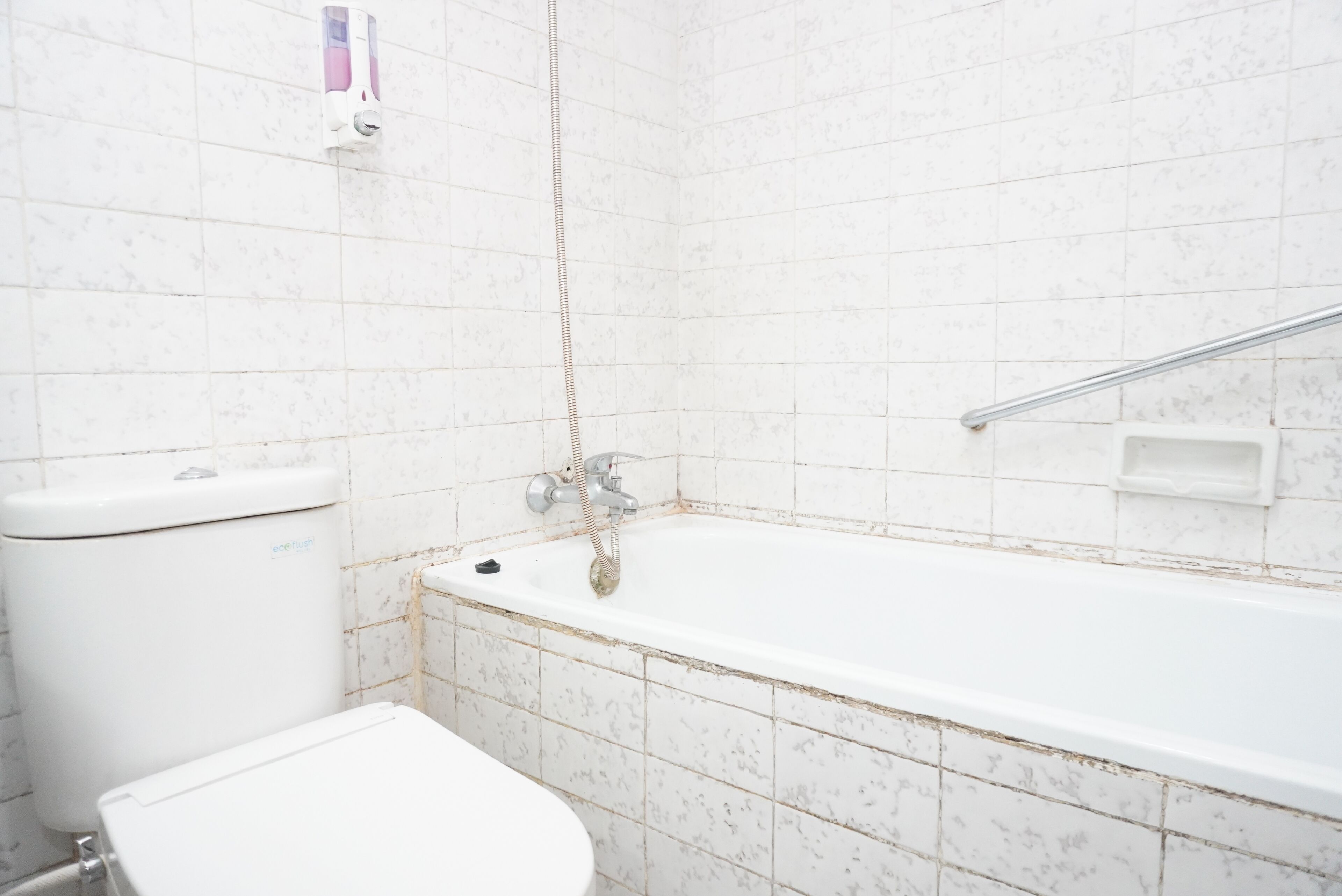 Een badkamer met een witte badkuip, een toilet en een handzeepdispenser aan de muur.