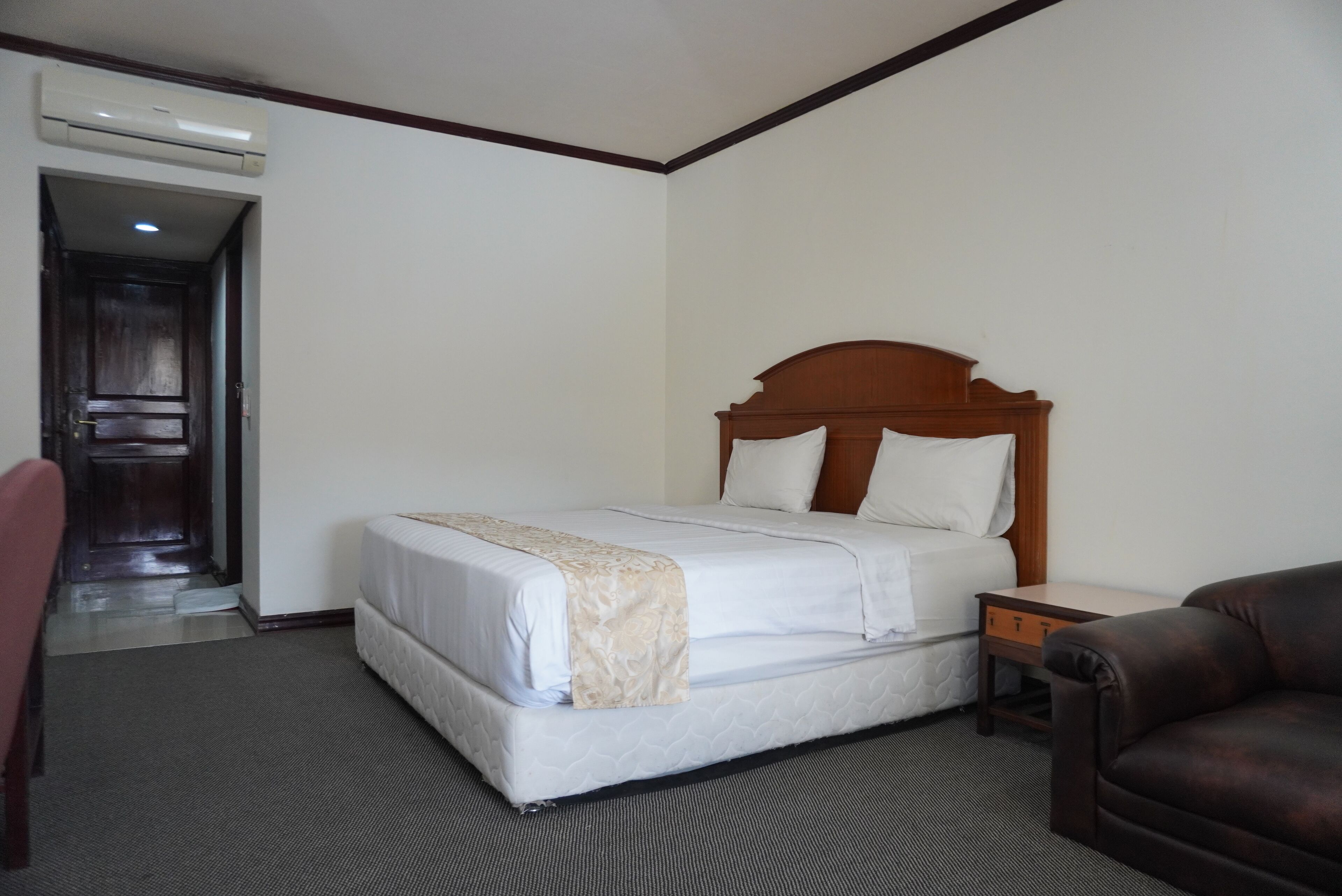 A hotel room with a bed, a nightstand, a chair, and a door leading to another room.