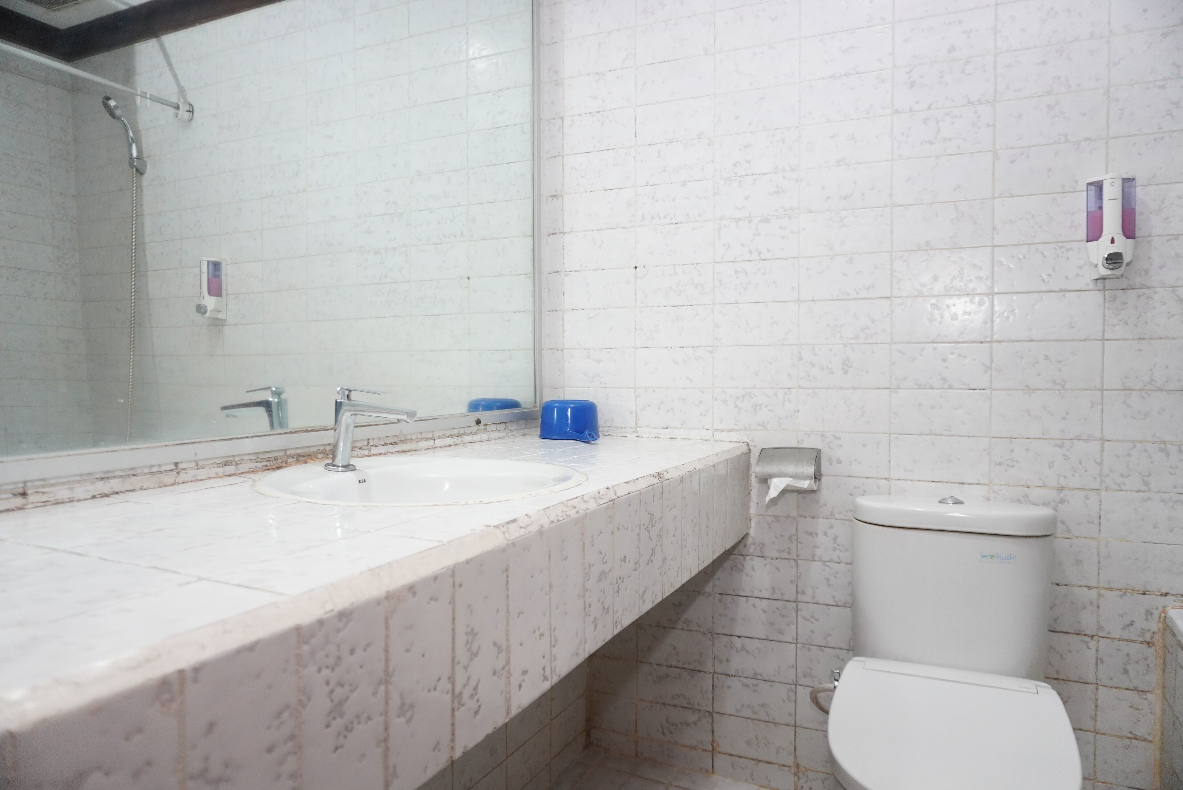 Un baño con lavamanos blanco, espejo, inodoro y dispensador de jabón.