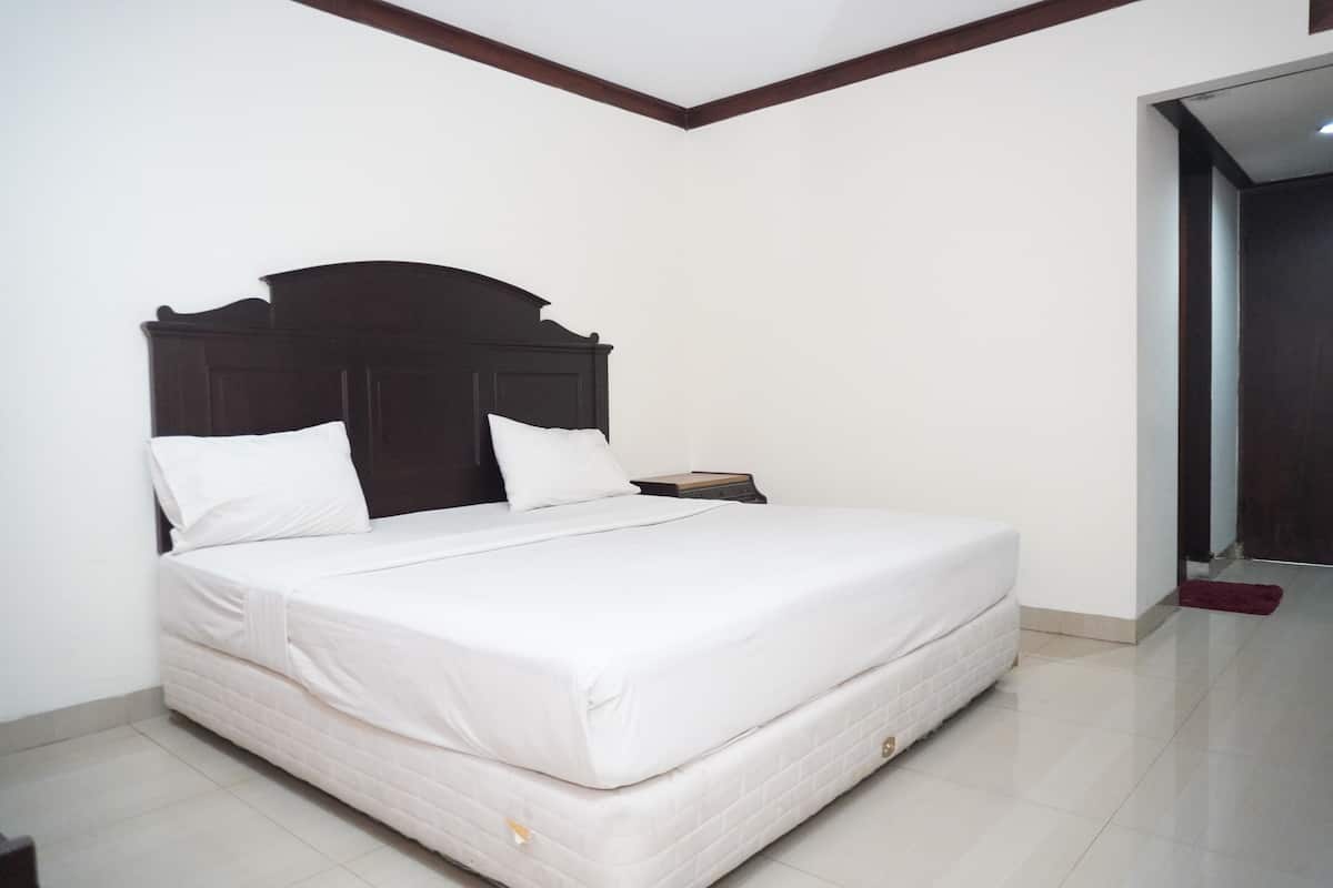 A neatly made bed with a dark headboard, a white mattress, and a single pillow.