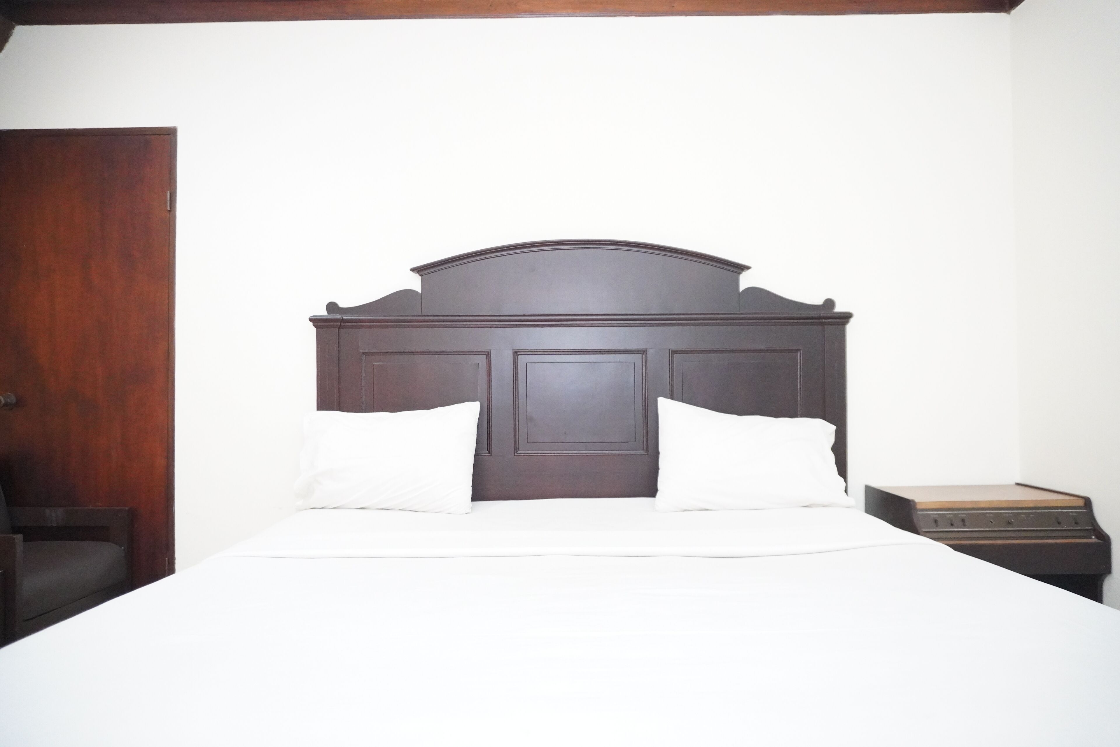 A bed with a wooden headboard, a wooden nightstand, and a wooden door.