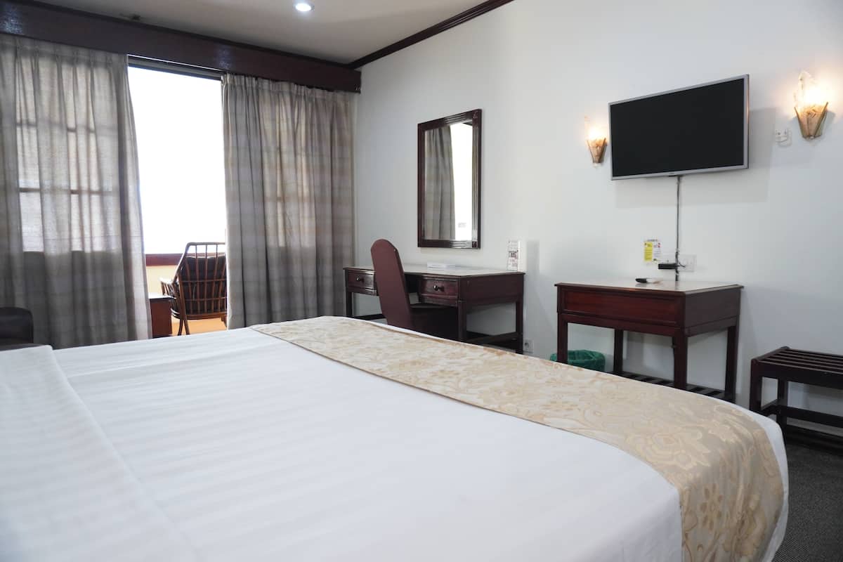 A hotel room with a large bed, a desk, a chair, a television, and a balcony with curtains.