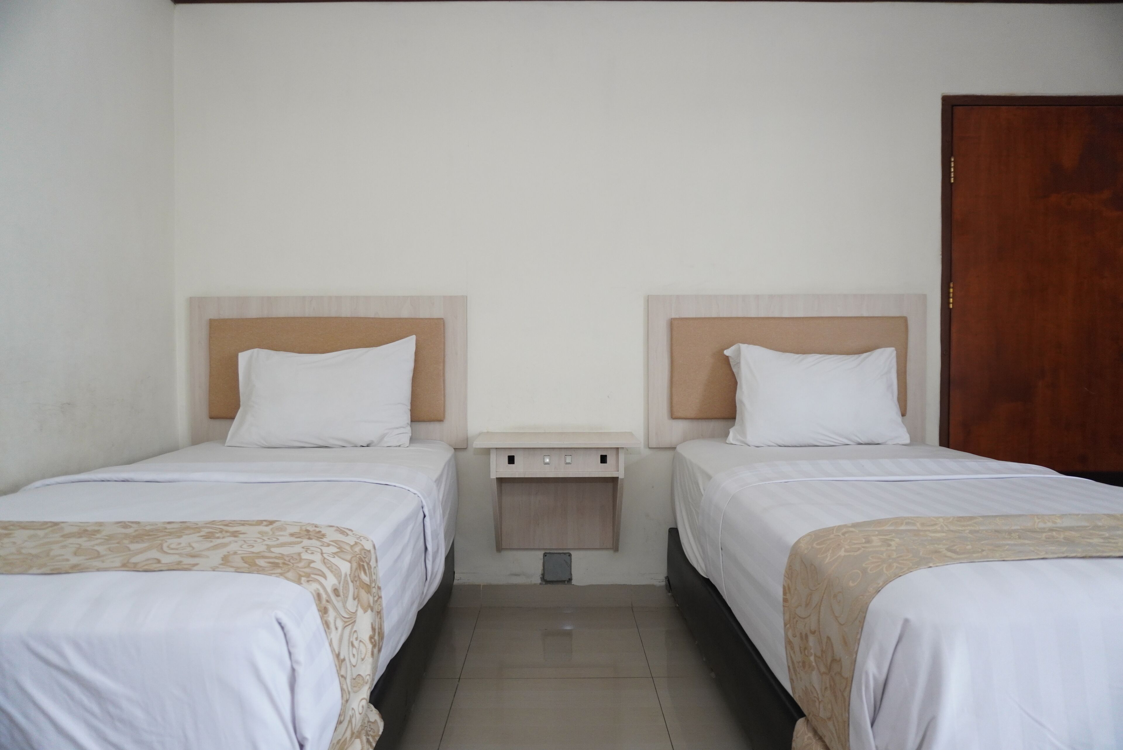 Ein Hotelzimmer mit zwei Einzelbetten, einem Holzkopfteil, einem kleinen Nachttisch und einer Holztür.