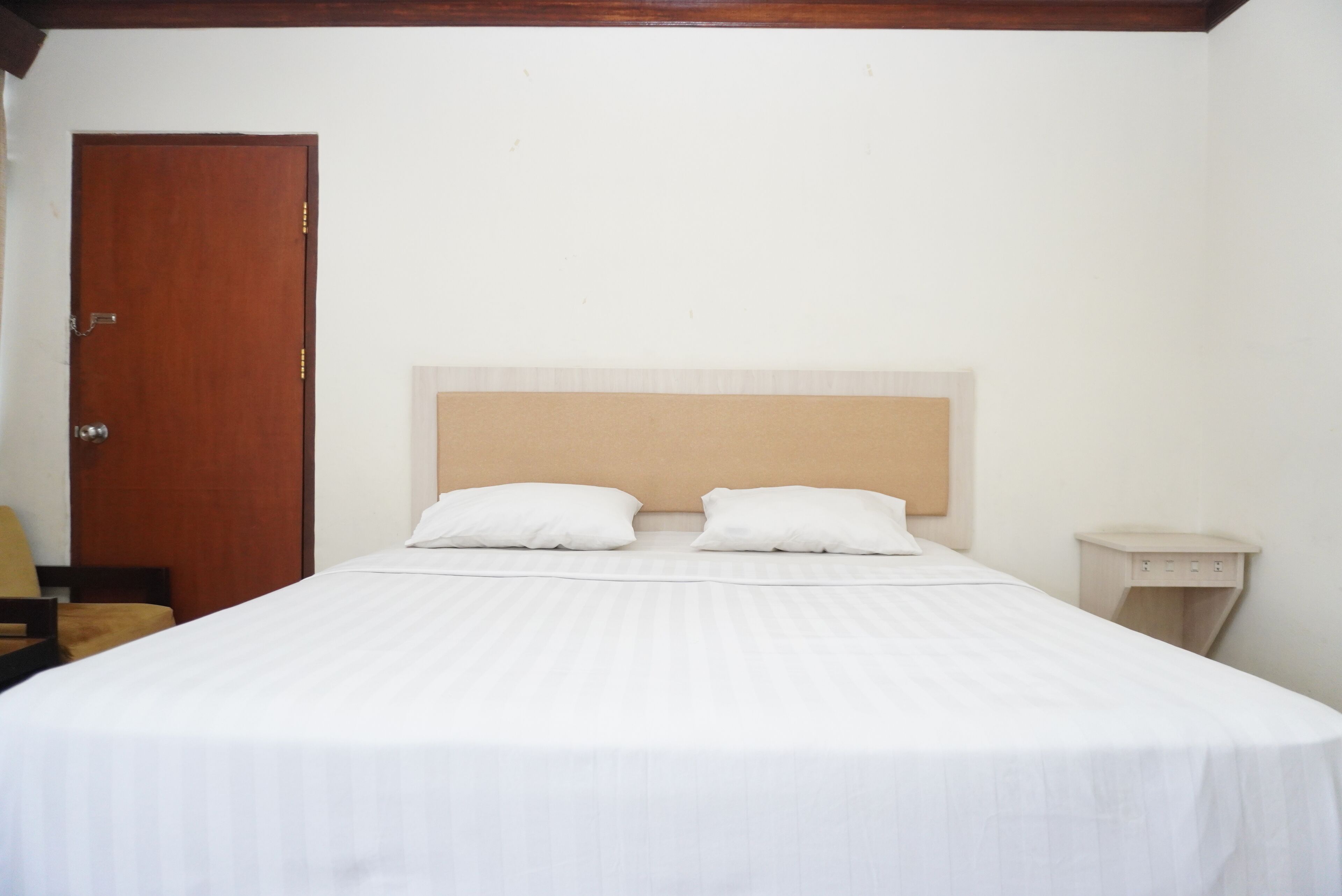 A neatly made bed with two pillows, a wooden door, and a small bedside table.
