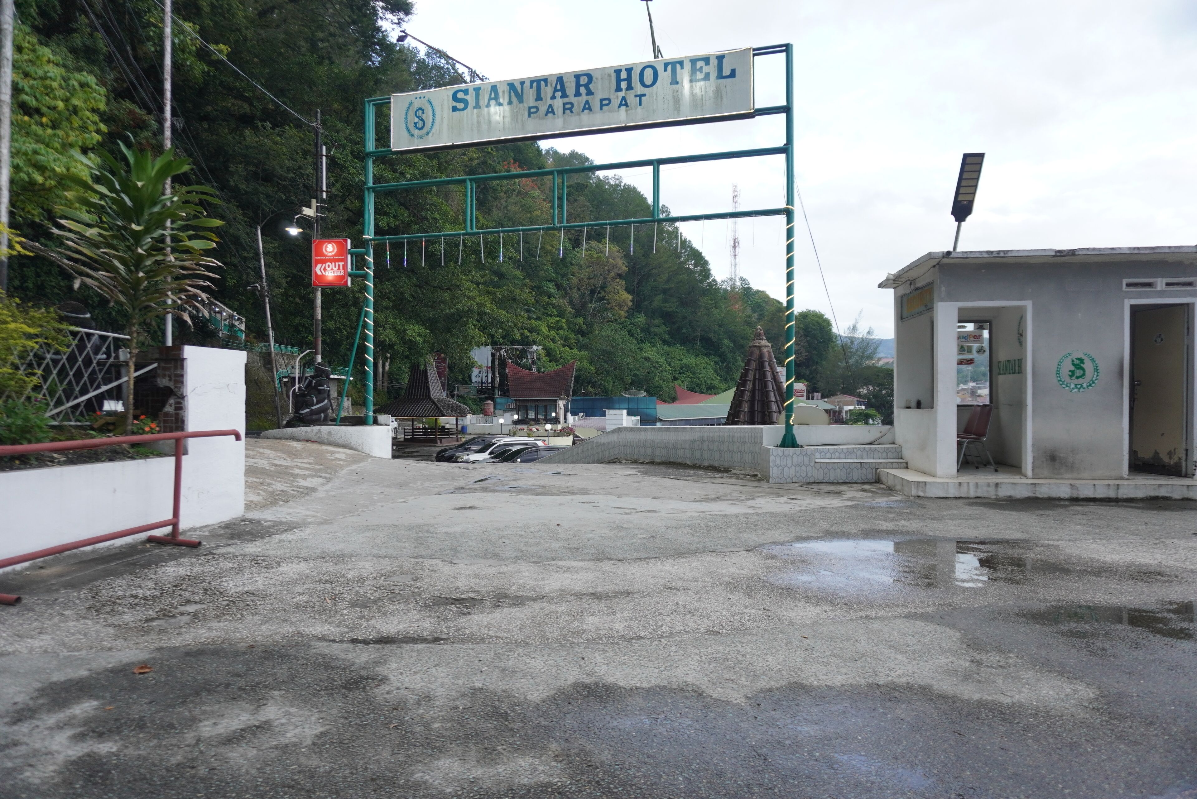 Der Eingang zum Siantar Hotel in Parapat, mit einer auffälligen Schilderung, einem kleinen Empfangsbereich und einem Parkplatz.