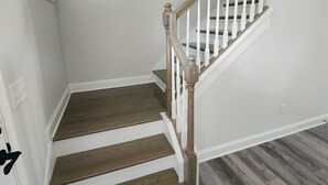 Een trap met houten treden en witte leuningen, die uitkomt op een plateau met een lamp.