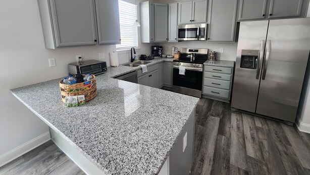 Een moderne keuken met grijze kastjes, een granieten aanrechtblad, roestvrijstalen apparatuur en een centraal eiland.