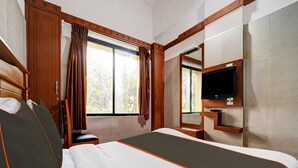 Une chambre d’hôtel avec un grand lit, une tête de lit en bois, un téléviseur fixé au mur et une fenêtre avec des rideaux.
