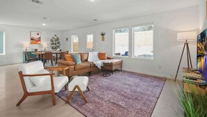 A spacious living room with a large sofa, a coffee table, and a dining area with chairs and a table. - The Oak Tree House 4 KING Beds! (San Antonio)