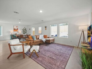 A spacious living room with a large sofa, a dining area, and a view of the backyard. - The Oak Tree House 4 KING Beds! (San Antonio)