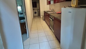 A narrow kitchen with a washing machine, a refrigerator, and cabinets.