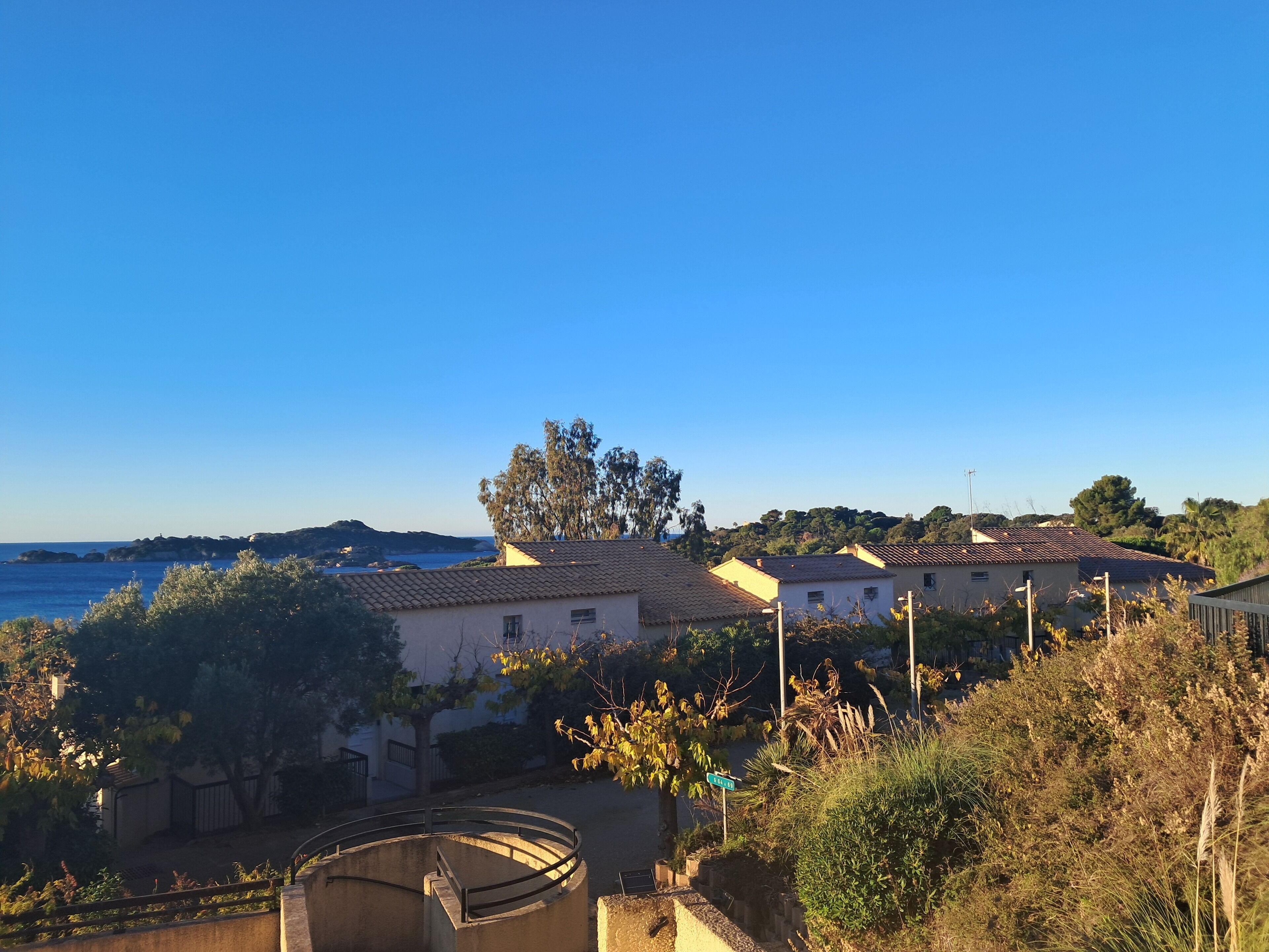 A residential area with houses, a clear blue sky, and a view of the sea.
