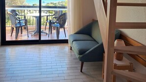 A room with a wooden staircase, a green sofa, a table with chairs, and a view of the sea through large glass doors. - VVF Hyères presqu'île de Giens (Hyères)
