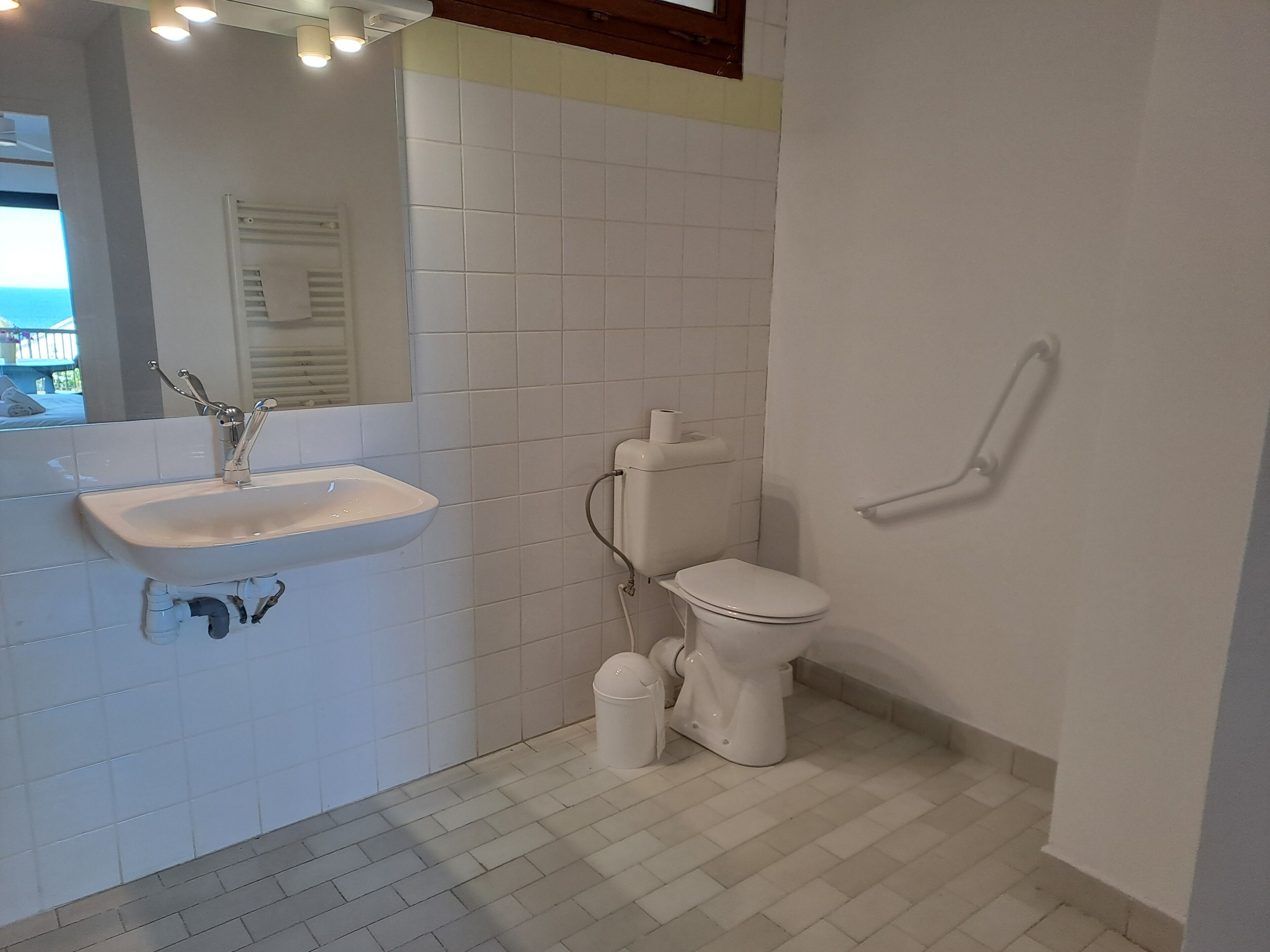Un baño con lavamanos, inodoro y bidé blancos, paredes con azulejos y una ventana visible.