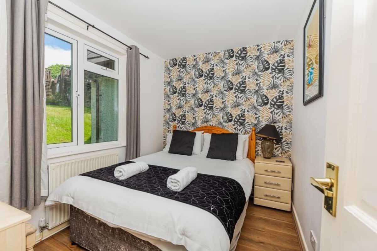 Ein Schlafzimmer mit einem Bett, einem Nachttisch, einem Fenster und einer Wand mit Muster.