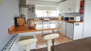 Een kleine keuken met witte kastjes, een houten aanrecht, een spoelbak, een magnetron en een kleine koelkast.