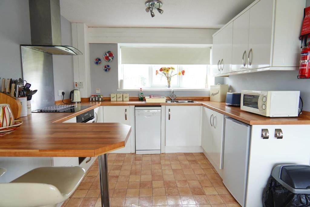 Una cocina compacta con armarios blancos, encimera de madera, lavavajillas integrado y microondas.