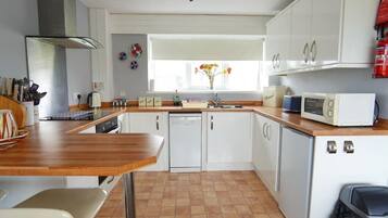 Una cocina compacta con armarios blancos, encimera de madera, lavavajillas integrado y microondas.