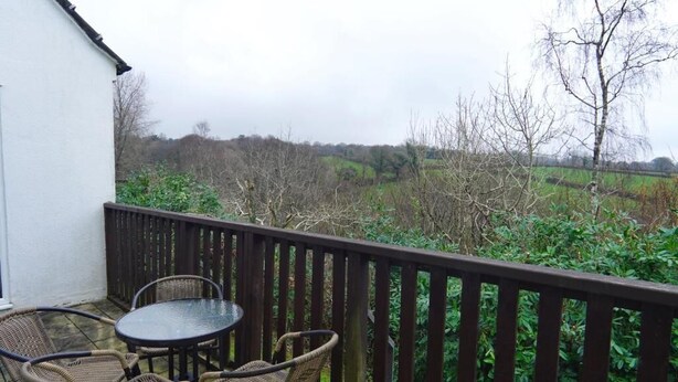 Een balkon met rieten meubels en een glazen tafel, met uitzicht op een landelijk landschap met bomen en velden.