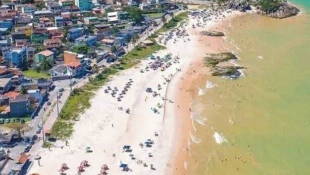 Luftaufnahme einer Küstenstadt mit Strand, der mit bunten Sonnenschirmen und einem dicht bebauten Wohngebiet gesäumt ist.