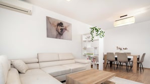 A modern living room with a beige sectional sofa, a wooden coffee table, and a dining area with a white table and chairs. - Family Apartment in the Center | 3 Bedrooms and Air Conditioning (Rzeszów)
