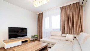 A modern living room with a flat-screen TV, a wooden coffee table, a beige sofa, and a potted plant. - Family Apartment in the Center | 3 Bedrooms and Air Conditioning (Rzeszów)