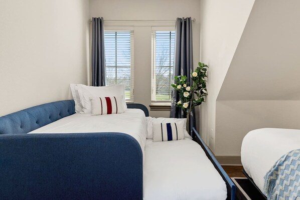 A bedroom with two beds, a window with curtains, and a vase with flowers.