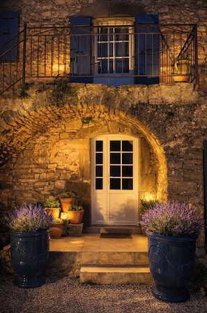 Un edificio de piedra con una puerta blanca, contraventanas azules y macetas de lavanda.