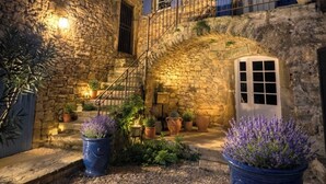 Un edificio de piedra con una escalera que lleva a un balcón, plantas en macetas y un patio de grava.