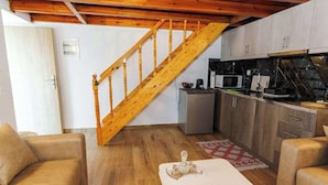 Ein kompakter Wohnraum mit einer Holztreppe, einer Küchenzeile und einer Essecke mit Tisch für zwei Personen.