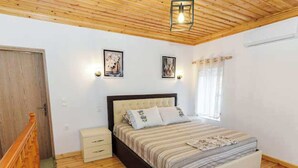 Ein Schlafzimmer mit Holzboden, einem Bett mit gestreifter Bettdecke, zwei Wandleuchten und einem Fenster mit Vorhängen.
