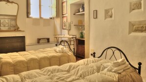 A bedroom with two beds, a dresser, a vanity, and a window with curtains. - Palazzo Bonaccorsi in the historic center with panoramic view (Colle di Val d'Elsa)