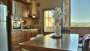 A kitchen with wooden cabinets, a stove, and a dining table with chairs. There is a vase with flowers on the table. - Palazzo Bonaccorsi in the historic center with panoramic view (Colle di Val d'Elsa)