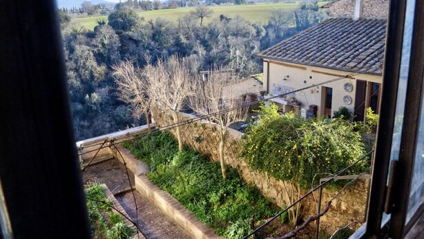 A view from a window overlooking a rural landscape with a house featuring a tiled roof and a garden area. - Palazzo Bonaccorsi in the historic center with panoramic view (Colle di Val d'Elsa)