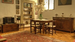 A cozy living room with a wooden table, chairs, a bookshelf, and a large window. - Palazzo Bonaccorsi in the historic center with panoramic view (Colle di Val d'Elsa)